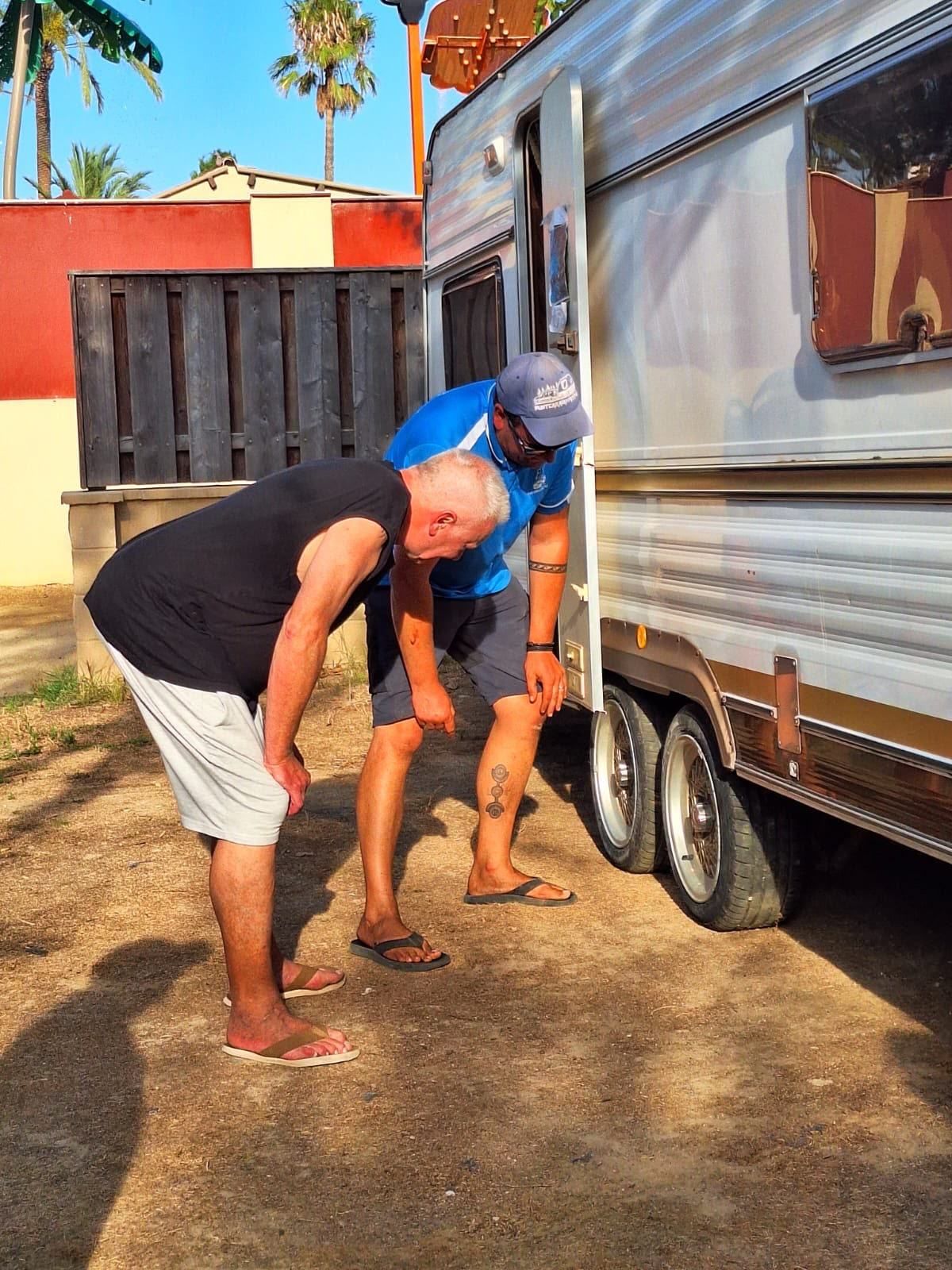 Two men checking the wheel of a twin-axle caravan